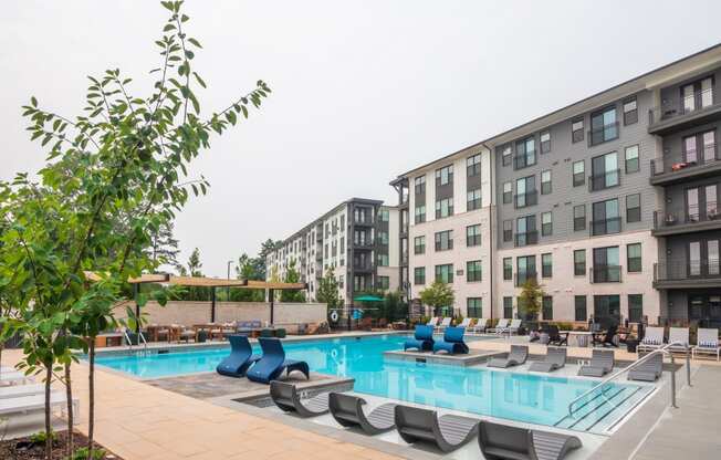 a swimming pool with lounge chairs in front of apartment buildings