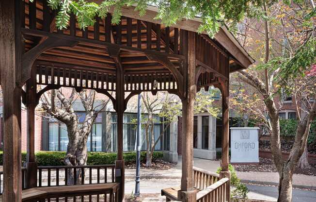 a wooden pavilion with benches in front of a building
