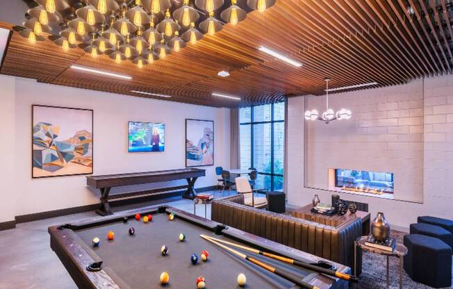 A pool table is in the middle of a room with a bench and a fireplace.