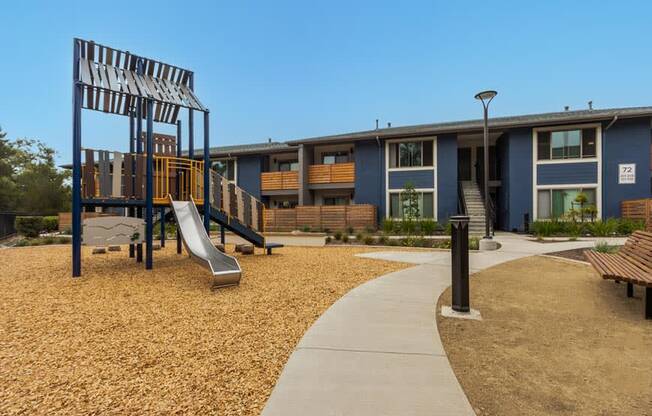 a playground with a slide and benches in front of a building