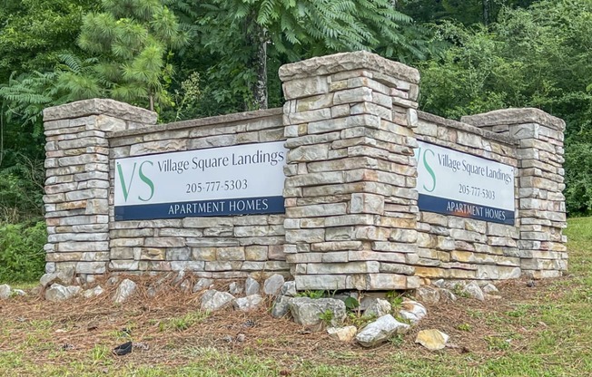 a stone pillar with signs on it in front of trees