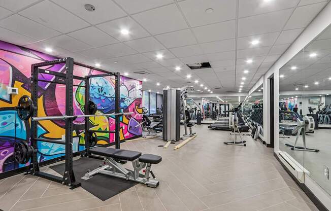 A gym with a variety of equipment and a colorful mural on the wall.