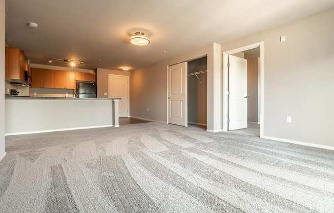 A large, empty room with a carpeted floor and a kitchen area in the background.