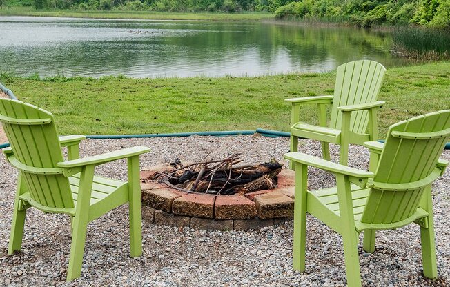 three green chairs sitting around a fire pit near a lake