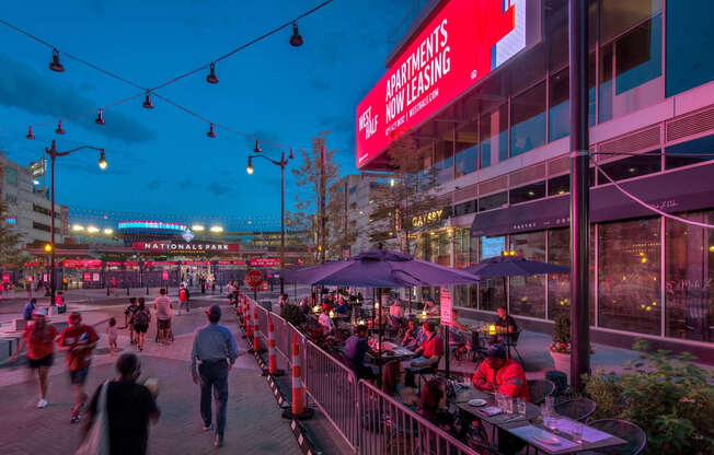 A busy outdoor bar scene with people walking and sitting at tables.