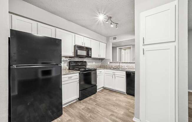 A black refrigerator stands in a kitchen with white cabinets and a black stove.