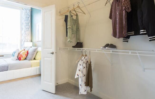 a closet with clothes hanging on a rack and a door to a bedroom