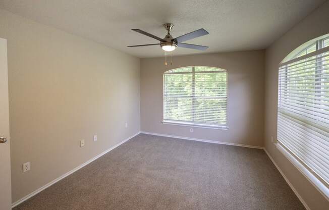 View of upstairs corner unit with two well lit windows, ceiling fan, and carpet flooring.