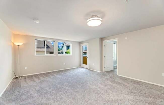 A spacious room with a carpeted floor and a window showing a view of other buildings.