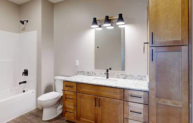 a bathroom with a light brown cabinets, a tall storage cabinet, quartz vanity sink, a mirror, and a shower and tub