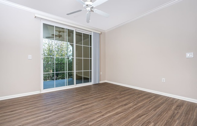 an empty living room with a sliding glass door and a ceiling fan