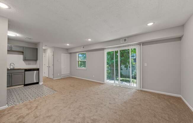 an empty living room with a large window and a kitchen