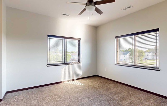 A bedroom with a ceiling fan, and two windows - one on each wall.