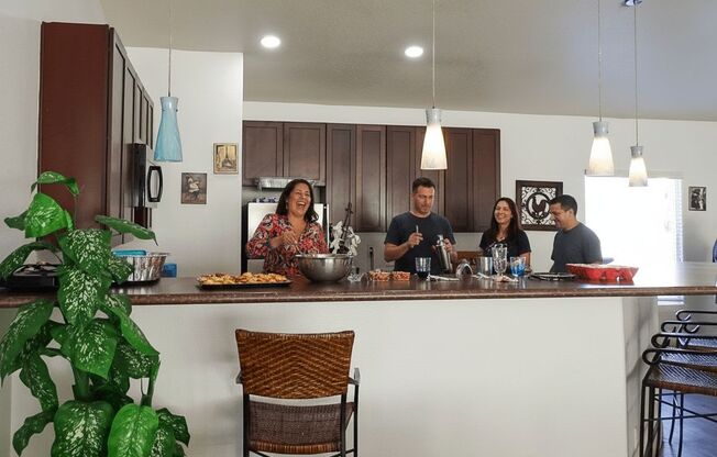 A group of people are gathered around a kitchen island with food and drinks on it.