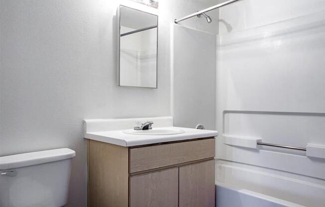 Bathroom with White Counter, Blonde Wood  Cabinets Next to Bathtub with Shower