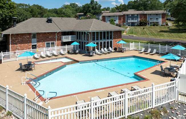 A white fence surrounds a pool with a building in the background.
