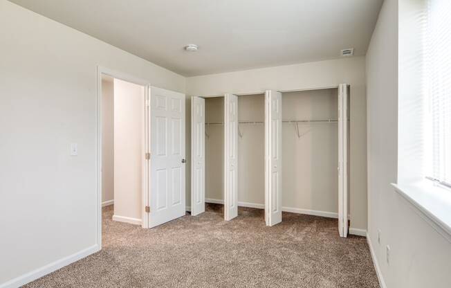 an empty bedroom with closet doors and a window