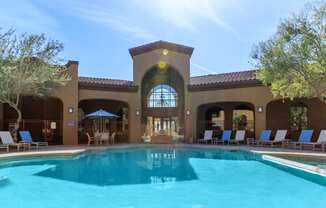 a resort style swimming pool with lounge chairs and umbrellas