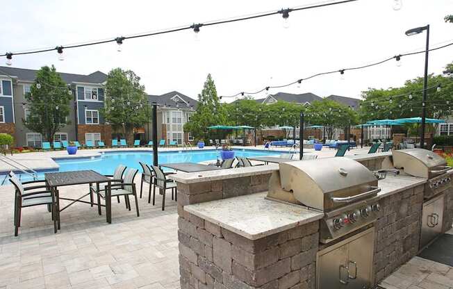 A pool with a barbecue grill and chairs is surrounded by apartment buildings.