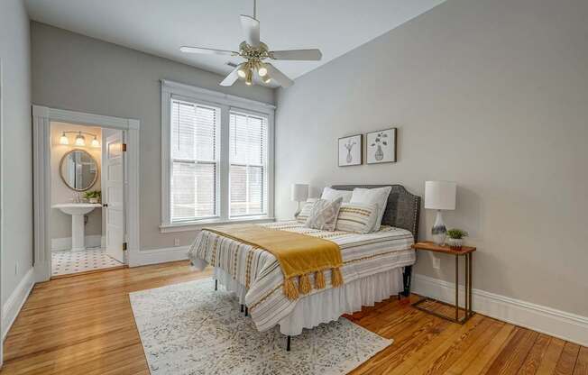 A bedroom with a bed, a ceiling fan, and a small table with a lamp.