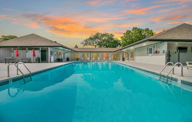 A large swimming pool in front of a building with a sunset in the background.