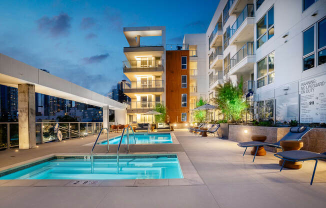 an outdoor swimming pool with chaise lounge chairs and a building in the background