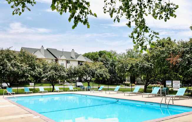 A large swimming pool surrounded by trees and lawn chairs.
