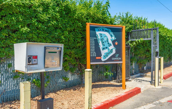 a sign with a map and a ticket machine in front of a hedge