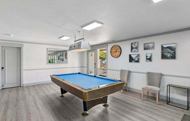A pool table in a room with a clock and pictures on the wall.