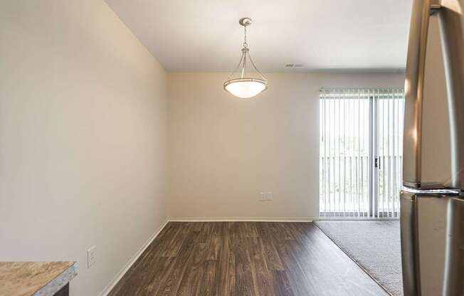 A kitchen with a refrigerator, wooden floors, and a hanging light fixture.