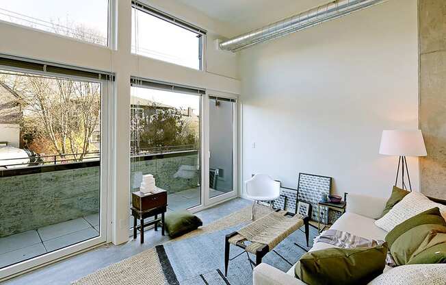 Living room with concrete flooring, floor to ceiling windows and a private outdoor patio. Inside is staged with a coffee table, rug and chair.at 19th & Mercer, Washington