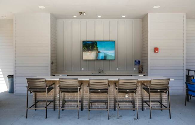 A television is mounted on a wall above a counter with four chairs in front of it.