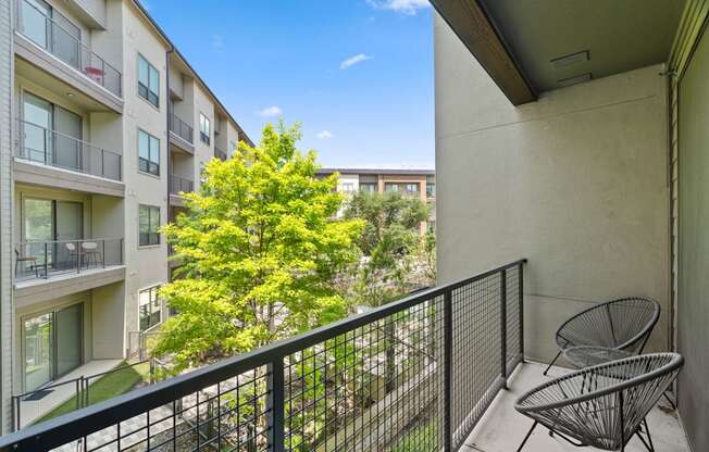 A balcony with a chair and a tree in the background.