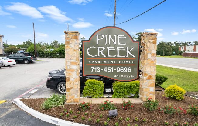 a sign for pine creek apartment homes in front of a parking lot