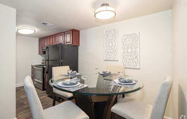 a dining area with a glass table and chairs and a kitchen in the background