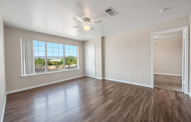 an empty living room with a large window and a ceiling fan
