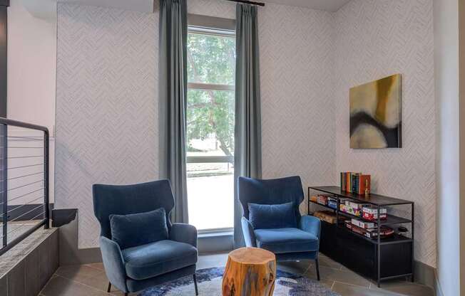Two blue chairs are in front of a window with a grey curtain.