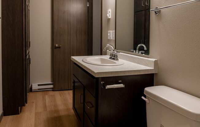 A bathroom with a toilet and a sink and a mirror. Fargo, ND Granger Court Apartments.