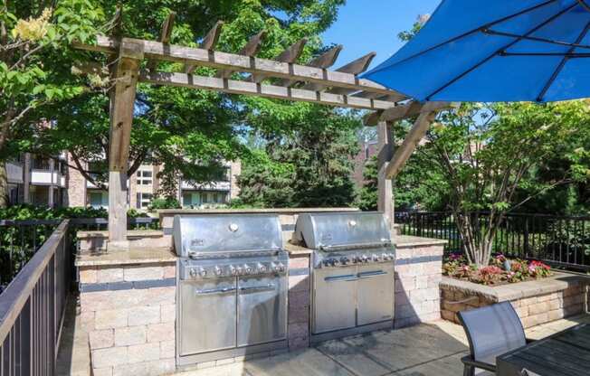 two stainless steel barbecue grills under a pergola on a patio