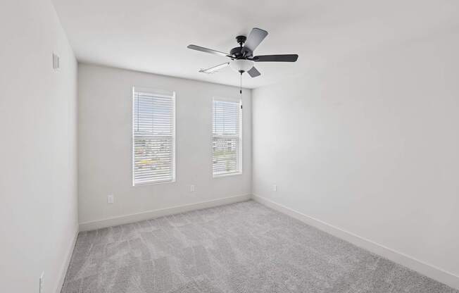 A room with a ceiling fan and two windows with blinds.
