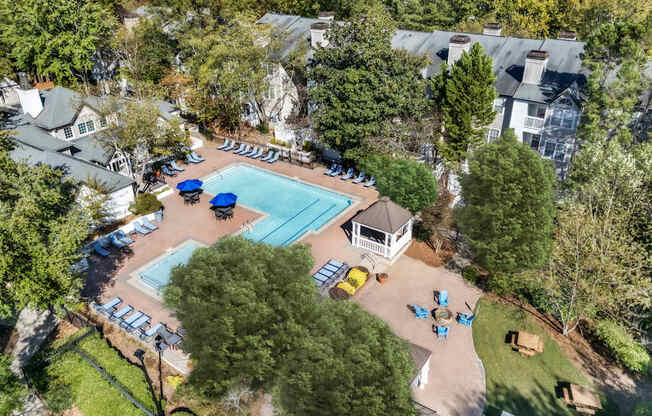 An aerial view of a swimming pool surrounded by trees and a small building.
