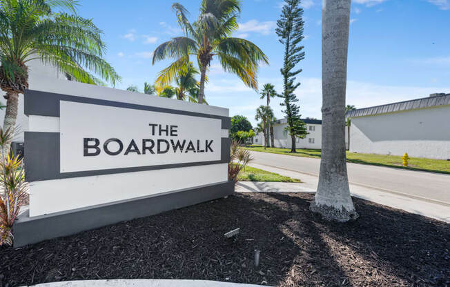 a sign for the boardwalk on the side of a road with palm trees