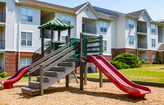 a playground with two slides in front of an apartment building