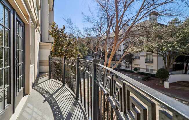 A balcony with a black railing and a view of a tree and a building.