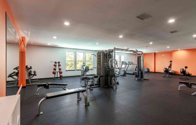 a gym with weights and cardio equipment on the floor and a window