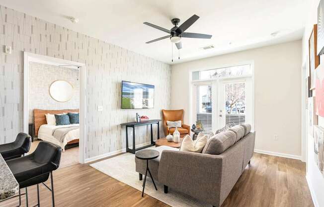 A living room with a grey couch, a black chair, and a white wall with a circular window.