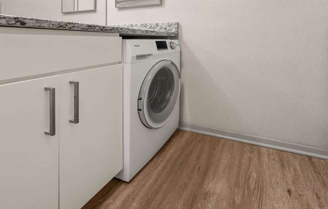 A white washing machine in a laundry room with wooden flooring.