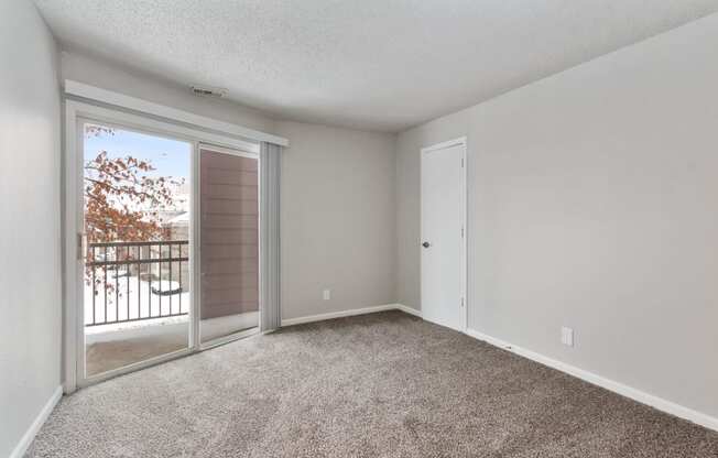 an empty living room with a sliding glass door to a balcony at Eastwood Crossings, Kansas City, Missouri