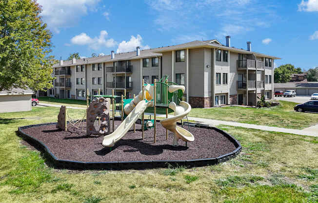 A playground with a slide and a merry-go-round in front of apartment buildings.