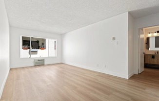 the living room and dining room of an apartment with white walls and wood floors